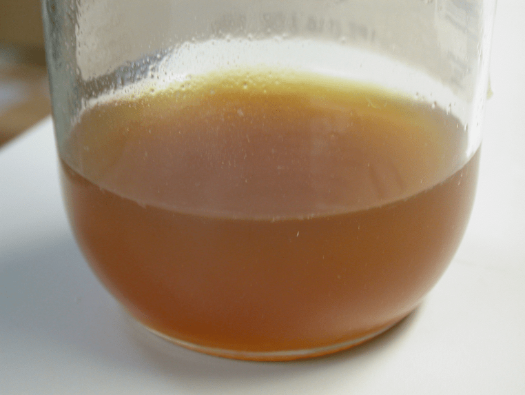 Picture of a jar of orange-ish liquid with some particles on the inner sides of the jar identified through FTIR analysis.