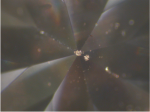 Chip damage at the apex of the back side of a gemstone, opposite the front facet, is shown at a magnification of 58 times. Additional chips can be seen, though out of focus. 